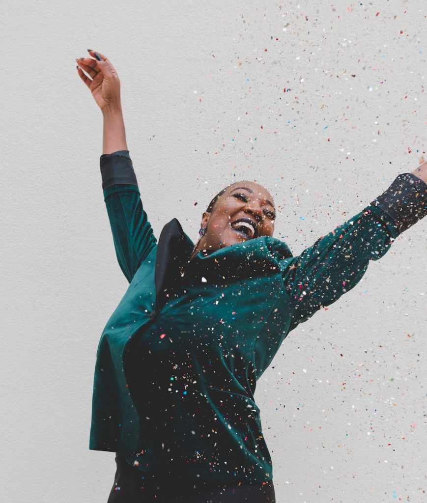 Moving Toward Your True Destiny? How to Tell | Happy As Annie. Martha Beck's "Shackles" test from Steering by Starlight (Black woman wearing teal suit with hands raised joyfully in air as confetti falls around her)