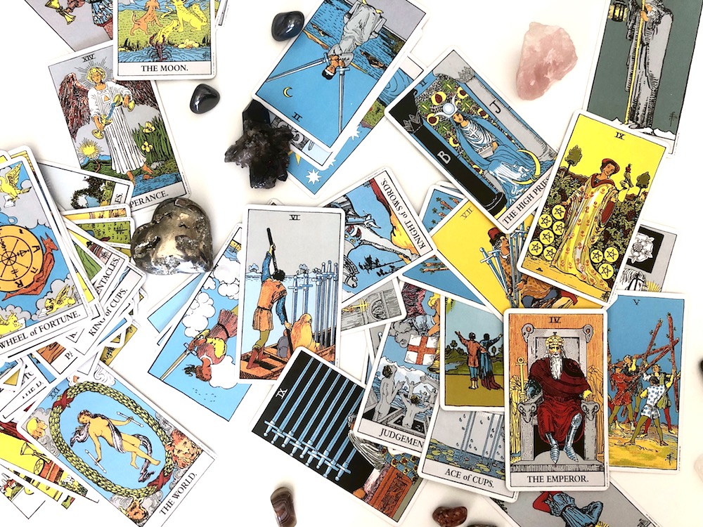 Happy As Annie | How to Bond with a New Tarot Deck - Bond with a new deck of tarot cards. Breaking in tarot cards. Connecting with your tarot cards. (Jumbled Rider-Waite tarot cards and diverse crystals laying on white table)