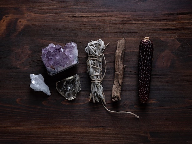 How to Break In and Cleanse Tarot Cards | Happy As Annie - How to Cleanse Tarot Cards with Crystals | There are so many ways to cleanse tarot decks. You can cleanse or bless a new tarot card with selenite or smoky quartz. (sage bundle, crystals, and other magical objects on wooden table)