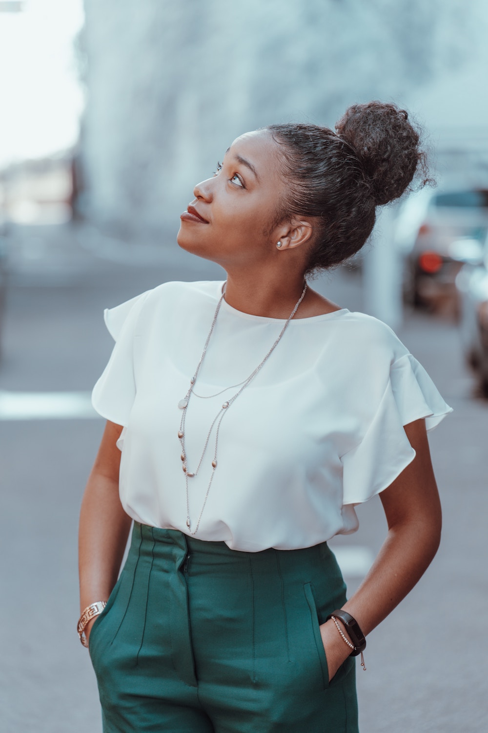 Set Better Goals: The One Question to Ask Yourself to Set More Aligned Goals | Happy As Annie | How to Set Better Goals (Black woman wearing whtie blouse and teal pants with hands in pockets looking up at sky)
