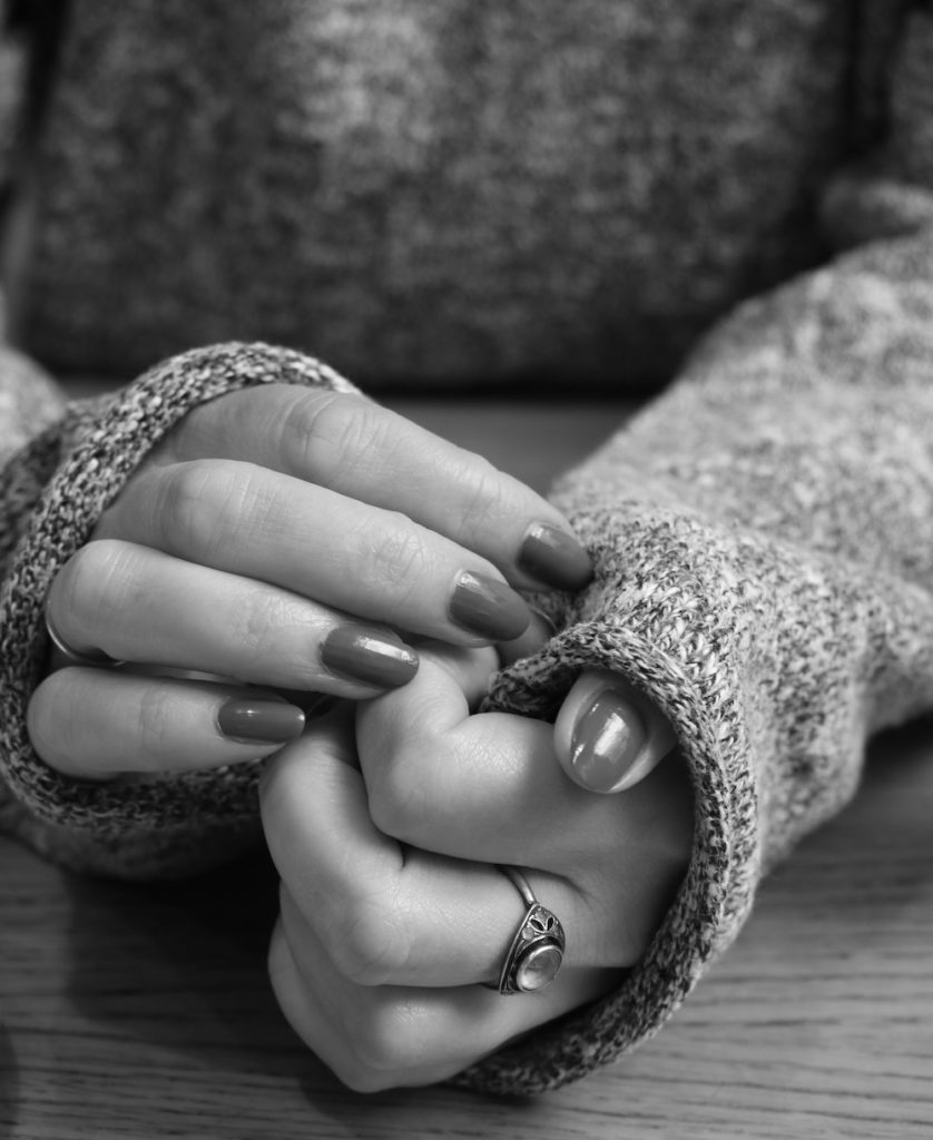 Grayscale photo of woman's hands together on wooden table, nail polish and ring