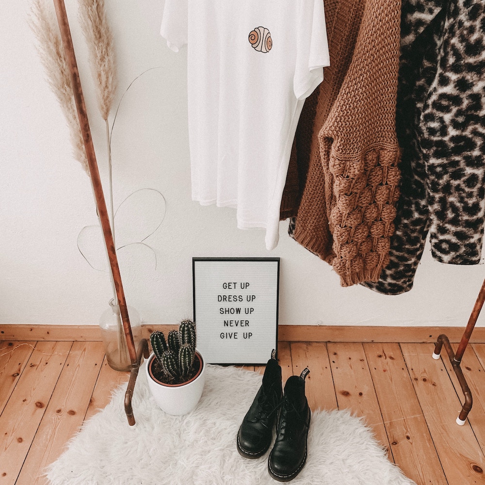 How to Discover Your Authentic Style | Happy As Annie (clothing rack with sweaters and t-shirt hanging above a pair of boots, potted cactus plant, and framed text art that says "GET UP DRESS UP SHOW UP NEVER GIVE UP")