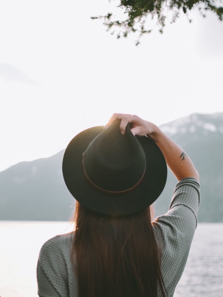 Woman wearing black hat looking off into distance with lake and mountain in background