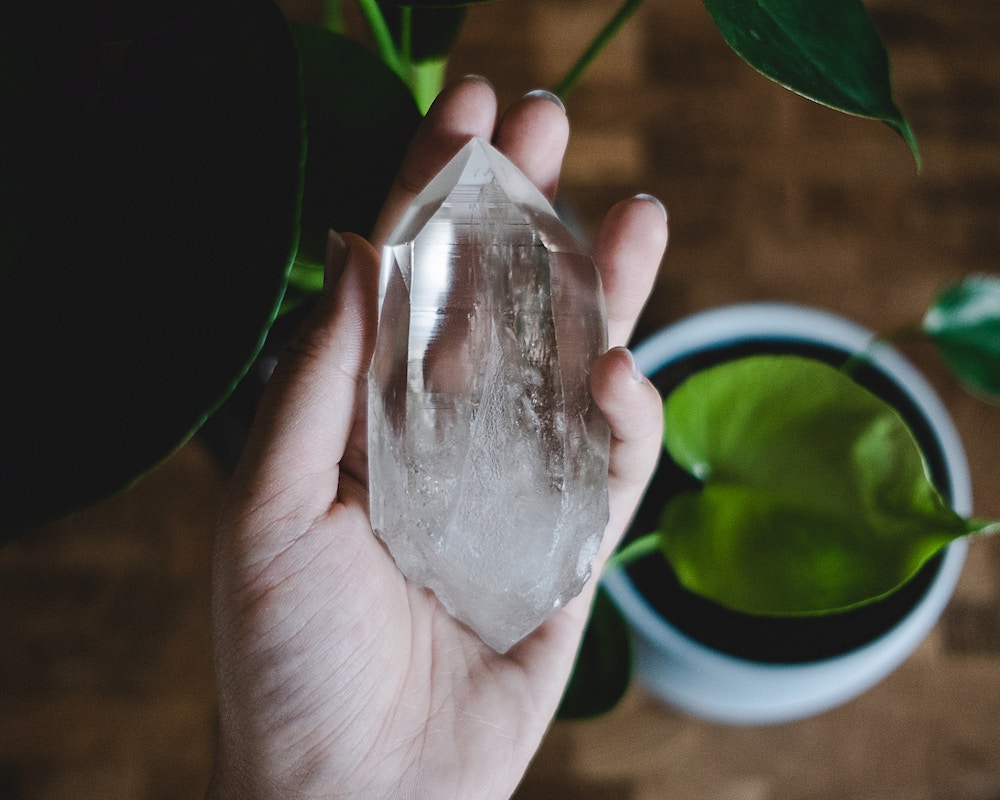 Clear quartz crystal in palm of woman's hand with plant in background