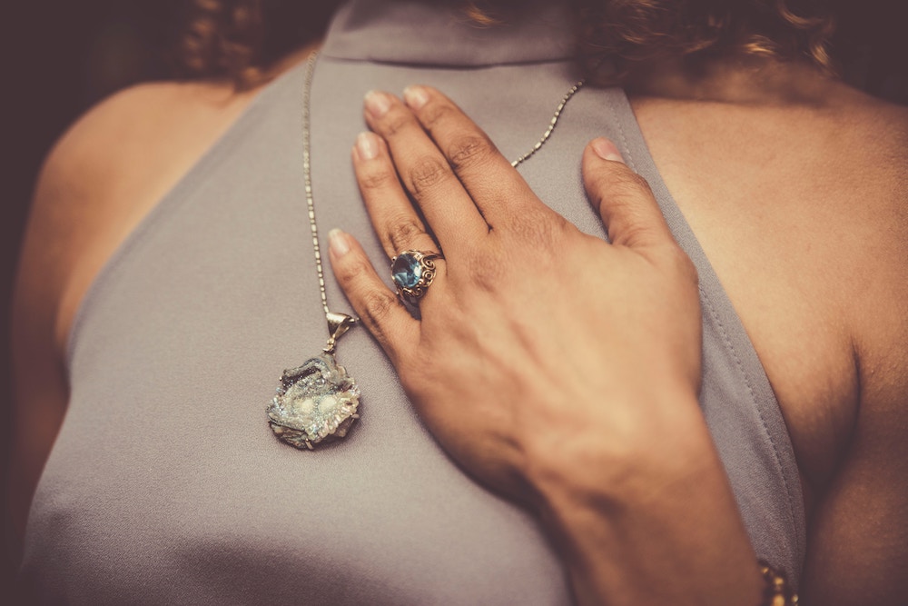 Woman placing hand over her heart wearing blue ring and crystal necklace