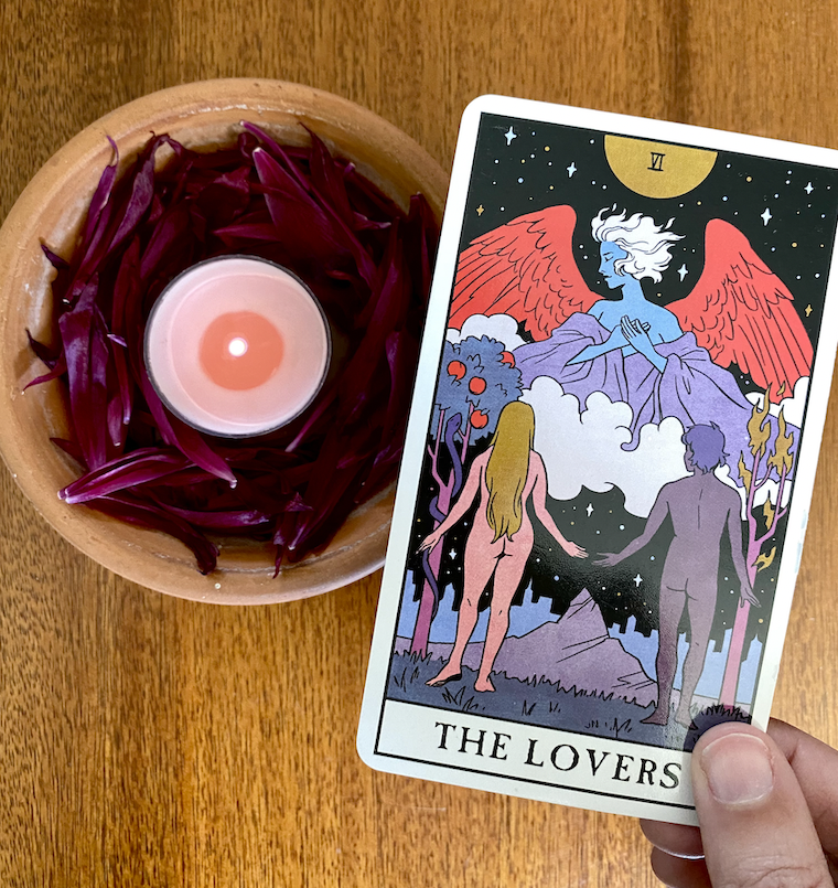 The Lovers Tarot Card in Modern Witch Tarot Deck with pink tea light and flower petals on wooden table