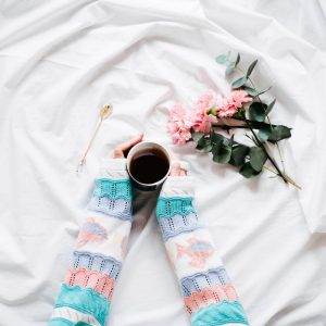 Girl in pastel colored knit sweater holding coffee mug against white sheets