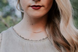 Woman with long blonde hair, red lips, and delicate necklace