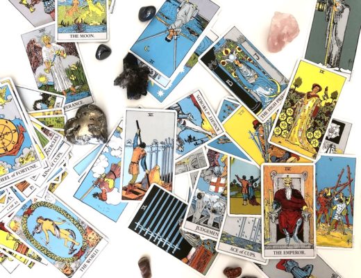 Jumble of Rider Waite tarot cards and crystals against white background