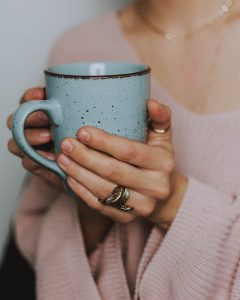 Girl in pink sweater holding blue mug with both hands, leaf ring