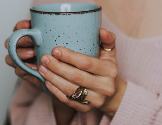 Girl in pink sweater holding blue mug with both hands, leaf ring