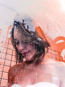 Woman standing in shower behind steamy glass door