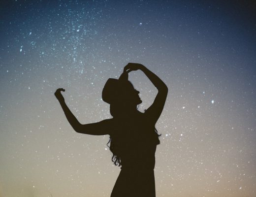 Woman's silhouette with arms up and wearing hat against starry sky background