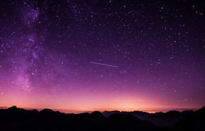 Shooting star across dark purple starry sky with mountains below