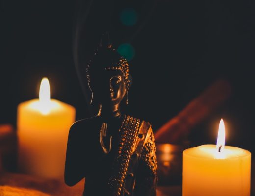 Small buddha figurine next to two lit votive candles