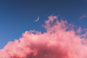 Thin crescent moon in blue sky with bright pink clouds