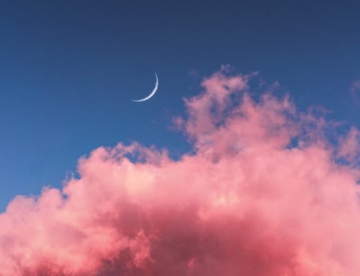 Thin crescent moon in blue sky with bright pink clouds