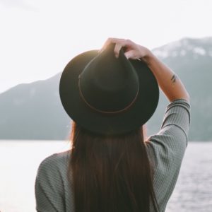 Woman wearing black hat looking off into distance with lake and mountain in background