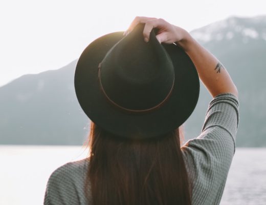 Woman wearing black hat looking off into distance with lake and mountain in background