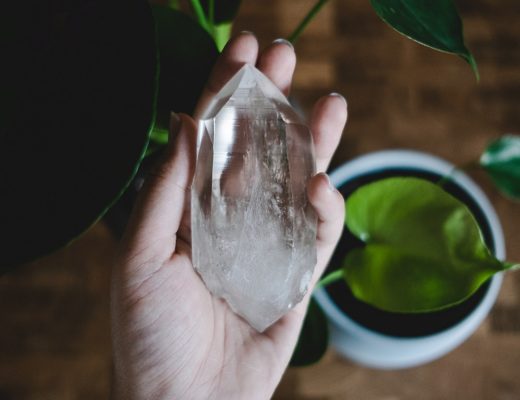 Clear quartz crystal in palm of woman's hand with plant in background