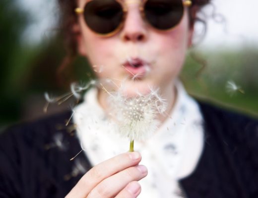 Woman wearing sunglasses blowing on dandelion