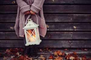 Girl wearing big purple cardigan and boots standing in fall leaves and holding white lantern