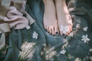Girls' bare feet on green blanket with black nail polish and white flowers scattered