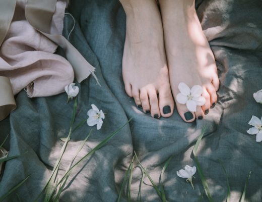 Girls' bare feet on green blanket with black nail polish and white flowers scattered