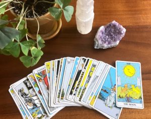 Rider Waite tarot cards fanned out with pictures facing up next to crystals and plant on wooden table