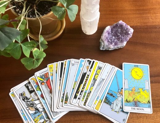 Rider Waite tarot cards fanned out with pictures facing up next to crystals and plant on wooden table