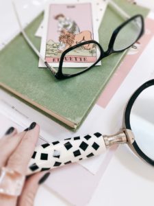 Strength tarot card in French sitting on book with glasses and magnifying glass