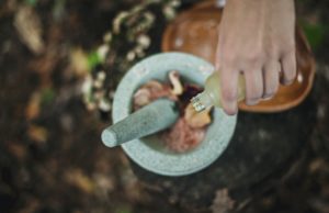 Hand pouring elixir into mortar and pestle to perform herbal magic spell